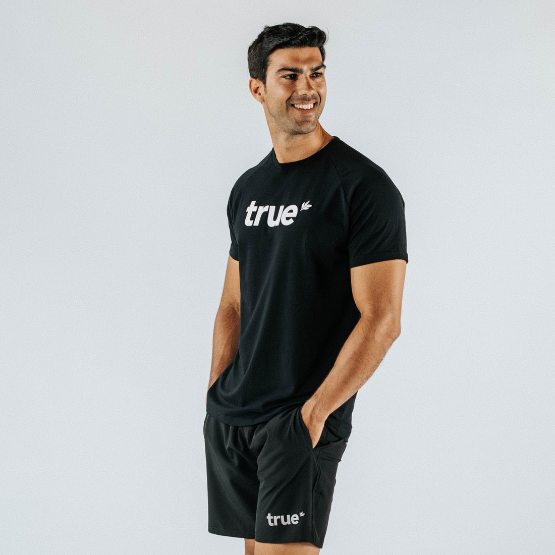 Men’s black “true” logo crewneck t‑shirt, athletic fit on male model — casual activewear product photo on light studio background.