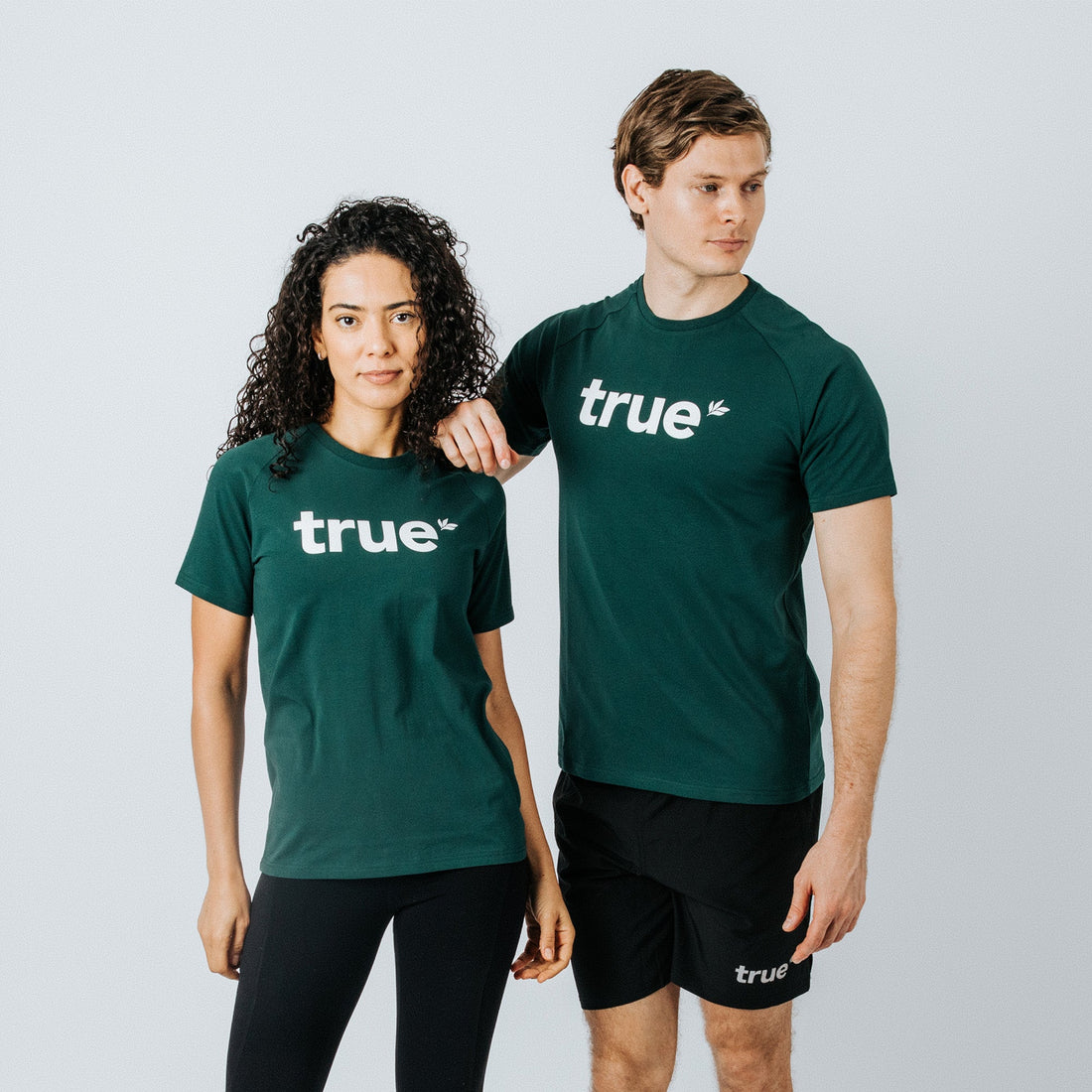 Two models (female and male) wearing forest-green "true" logo t-shirts — women&