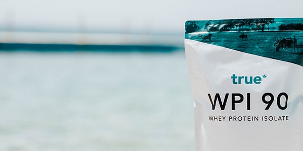 True WPI 90 whey protein isolate pouch on a seaside beach background — high-protein supplement pouch for fitness and recovery