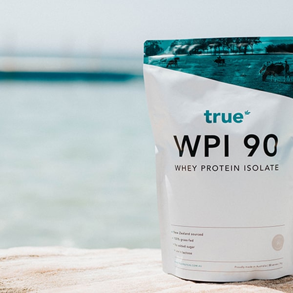 True WPI 90 whey protein isolate pouch by True Nutrition pictured on a sandy beach with ocean background