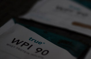 Close-up of True WPI 90 whey protein isolate pouch on a wooden surface, fitness supplement packaging for athletes and gym recovery