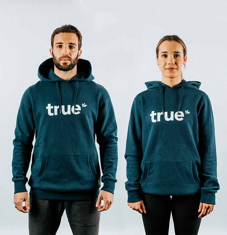 Navy unisex pullover hoodie with white "true" logo worn by male and female models, front view with drawstring hood and kangaroo pocket — product photo.