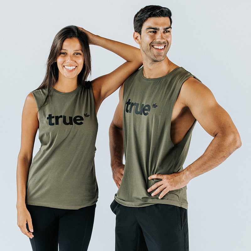 Two smiling models wearing khaki "true" logo sleeveless muscle tank tops and black workout shorts, studio shot, unisex athleisure fit for men and women.
