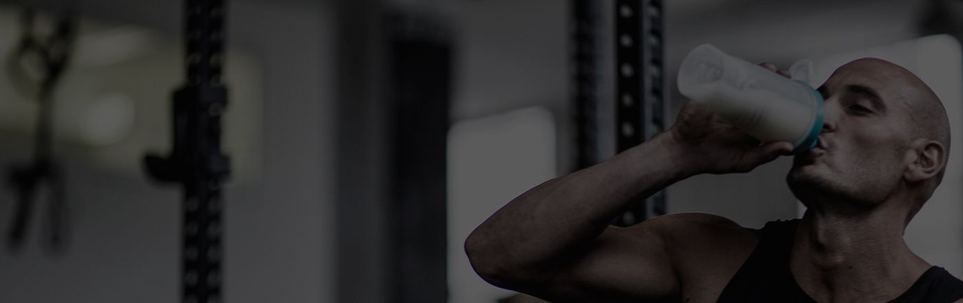 Muscular athlete in a gym drinking from a protein shaker bottle — rugby supplements banner promoting protein shakes and sports nutrition for rugby players.