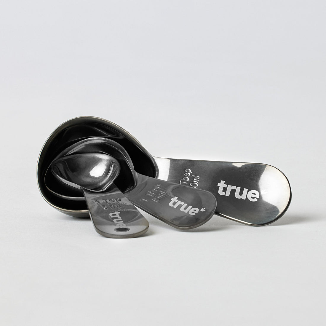 True brand set of four stainless steel nested measuring spoons with engraved sizes and logo on white background, product kitchen utensil photo