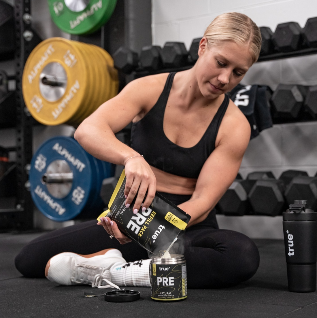 Muscular women crouching, in gym setting with a shaker 